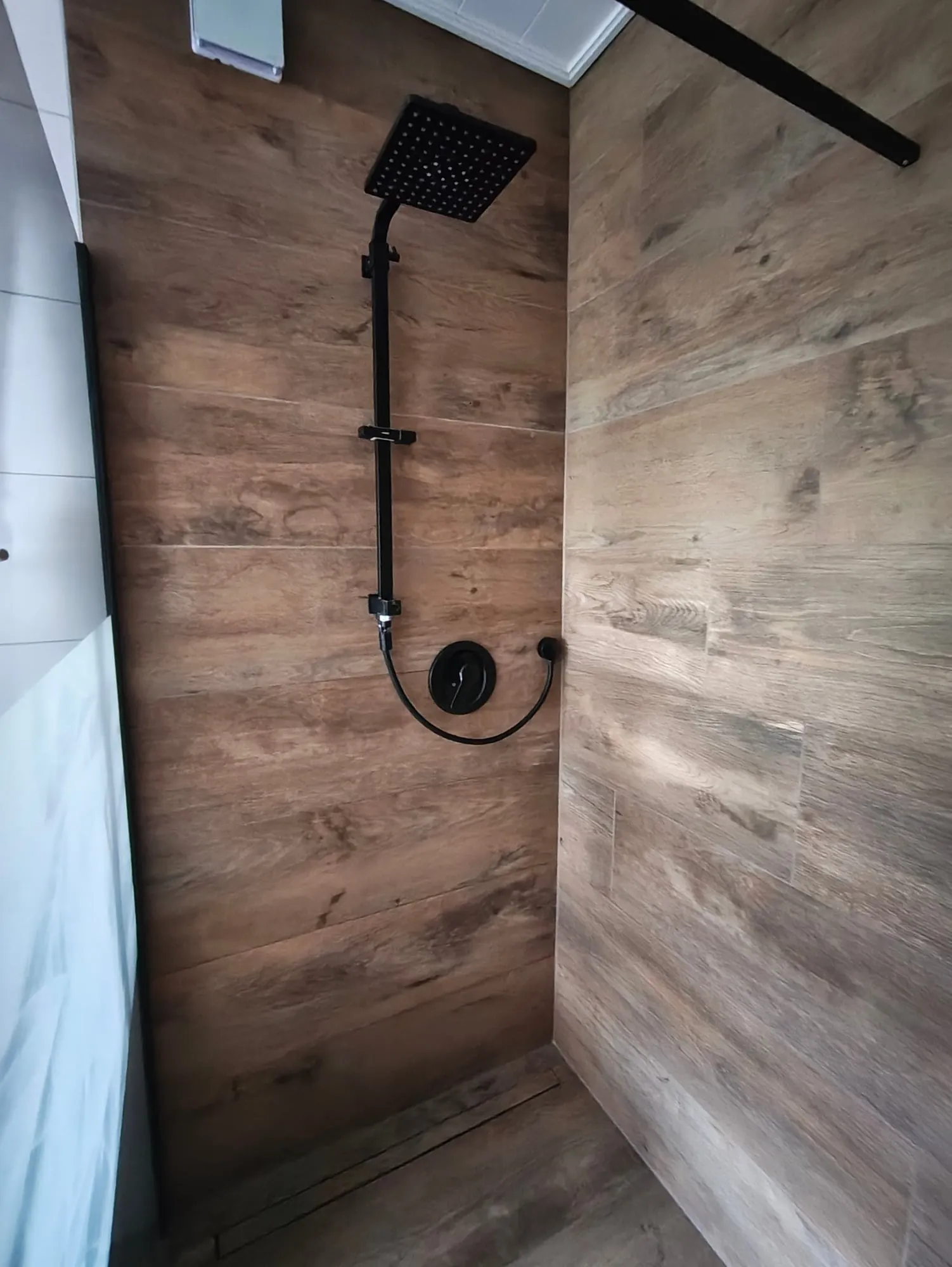 In der Dusche: Brause und Armatur an der Wand in Holzoptik, der Boden ebenerdig.