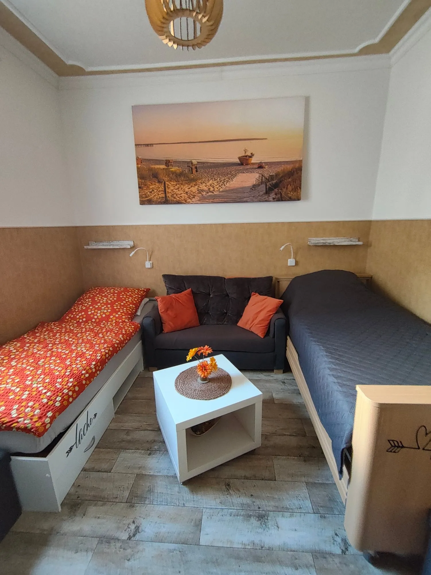 Zimmer 1: zwei Einzelbetten mit einem kleinen Sofa dazwischen, darüber ein Strandbild.
