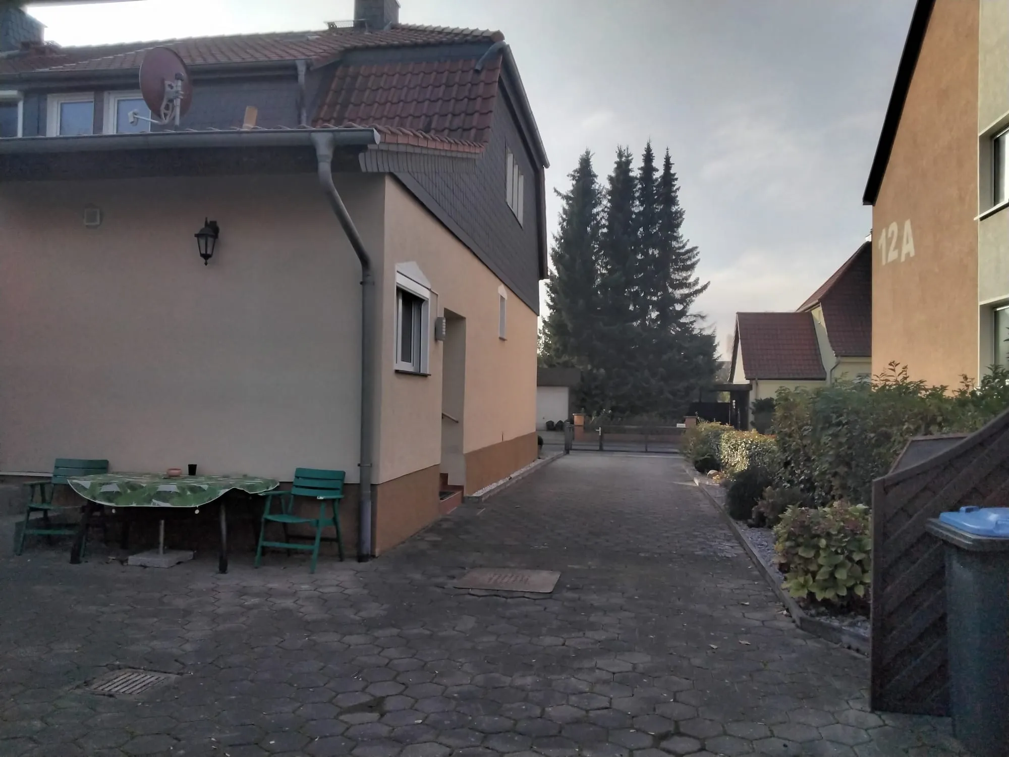 Die gepflasterte Einfahrt neben dem Haus, mit Platz zum Parken und einem Sitzplatz mit Tisch und Stühlen an der Hauswand.