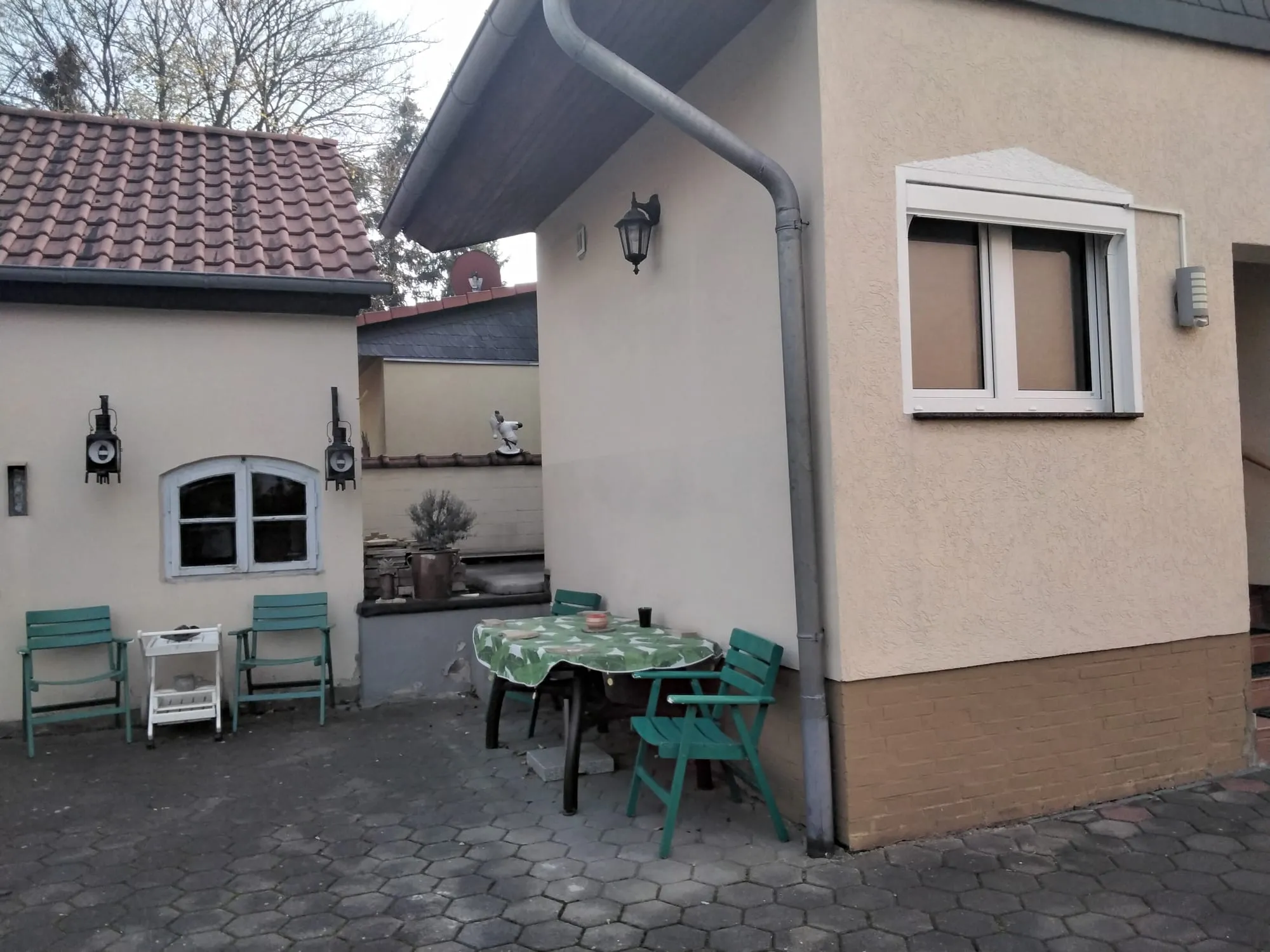 Sitzplatz hinter dem Haus: ein Tisch mit Decke und mehrere Klappstühle auf dem gepflasterten Hof.